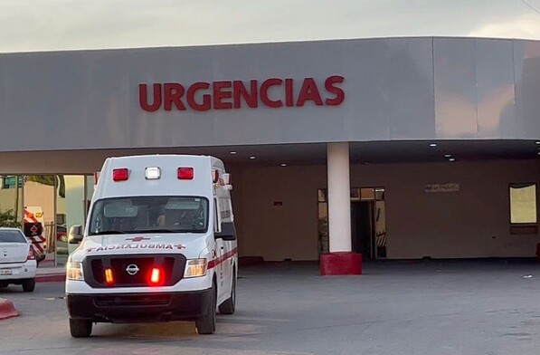 Se observa una ambulancia color blanco con rojo, está estacionada, afuera de un lugar que dice Urgencias.