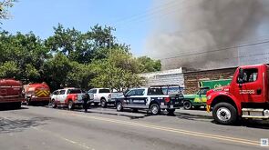 Camiones de bomberos y patrulla de la Policía de Guadalajara en medio de la calle con una columna de humo negro emanando de un incendio detrás