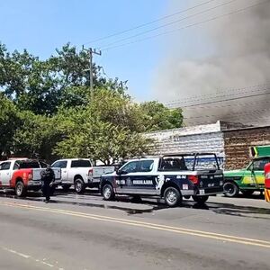 Camiones de bomberos y patrulla de la Policía de Guadalajara en medio de la calle con una columna de humo negro emanando de un incendio detrás