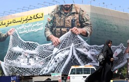 persona caminando afuera de un mural en el que se representa en sátira la situación de la guerra de medio oriente.