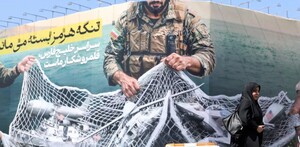 persona caminando afuera de un mural en el que se representa en sátira la situación de la guerra de medio oriente.