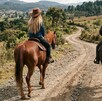 Se observa a una mujer y un hombre montando cada uno un caballo, sobre terracería.