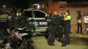 Oficiales alrededor de una patrulla de la Policía Municipal de Zapopan y moto patrullas al exterior de una zona de viviendas durante la noche