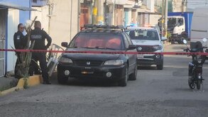 Policías esperando afuera de un domicilio junto a una cinta roja que impide el paso.