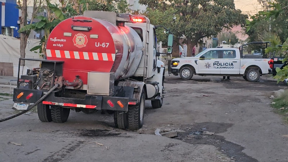 Camión de Protección Civil y Bomberos con una patrulla de la Policía Municipal de Tlajomulco estacionados en un área acordonada con casas alrededor