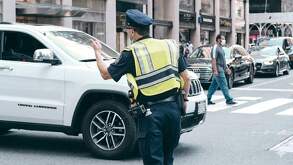 Un policía de tránsito con un chaleco amarillo en medio de una calle de una ciudad con una camioneta blanca frente a él