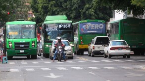 Cuatro camiones de transporte público en Guadalajara de distintas rutas circulando en una calle con autos y una motocicleta alrededor