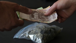 Manos intercambiando dinero junto a una bolsa de droga.