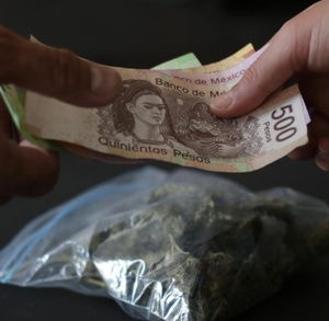 Manos intercambiando dinero junto a una bolsa de droga.