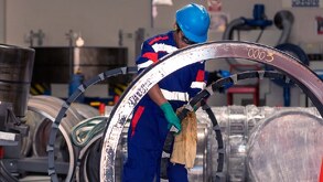 Trabajador con casco y lentes de seguridad limpiando un engrane gigante.
