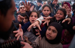 Familias desplazadas extienden las manos mientras esperan a recibir donativos de alimentos en un campamento después de huir de los bombardeos israelíes en el su