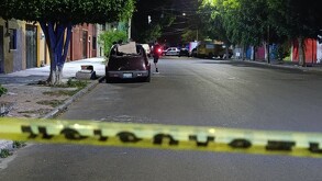 Cinta policiaca amarilla acordonando una calle con casas, una camioneta, una patrulla de la Policía de Guadalajara y un grupo de personas en la zona