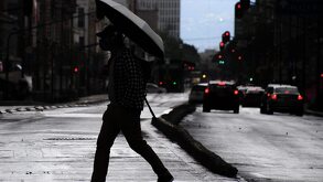 Un hombre cruza la calle mientras usa un paraguas para protegerse de la lluvia.