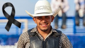 Se observa a un hombre joven que porta un sombrero vaquero y está sonriendo, hay un moño negro a lado.