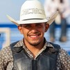Se observa a un hombre joven que porta un sombrero vaquero y está sonriendo, hay un moño negro a lado.