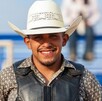 Se observa a un hombre joven que porta un sombrero vaquero y está sonriendo, hay un moño negro a lado.