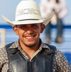 Se observa a un hombre joven que porta un sombrero vaquero y está sonriendo, hay un moño negro a lado.