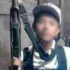 Niño con una gorra posa para una foto con un arma de grueso calibre entre sus manos.