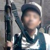Niño con una gorra posa para una foto con un arma de grueso calibre entre sus manos.