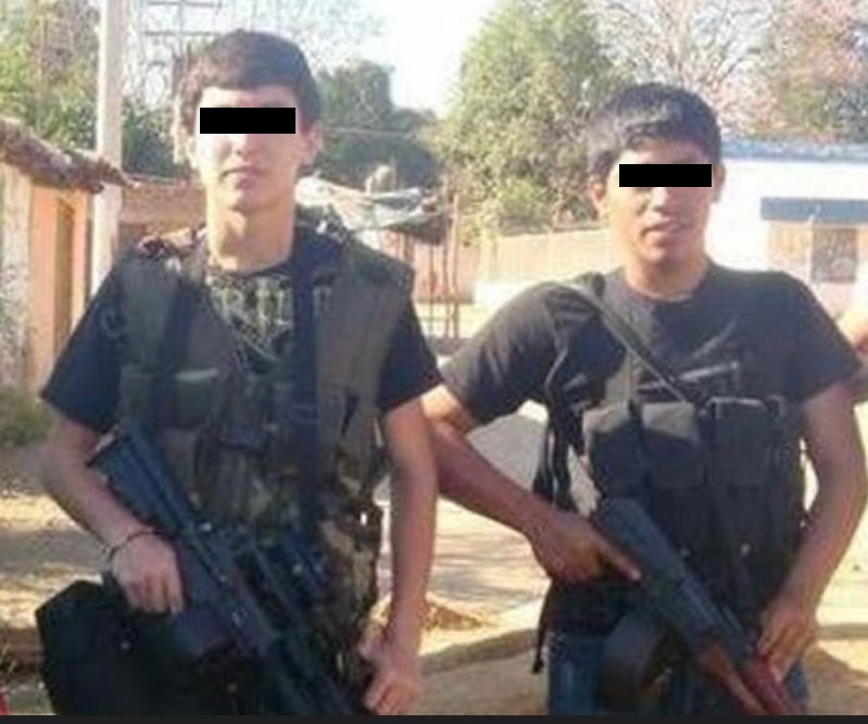 Dos jóvenes vestidos con ropa táctica posan para una foto cargando armas de grueso calibre.