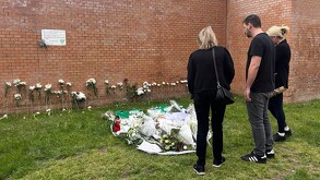 Vista del exterior del Centro Cultural La Despernada en Villanueva de la Cañada con personas vestidas de negro delante de ramos de flores y veladoras