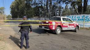 Policía parado junto a una patrulla en una zona acordonada con cinta de precaución.