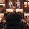 Javier Hernández, el Chicharito, vestido de negro sentado en un sillón con trofeos detrás.