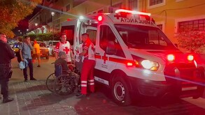 Ambulancia y tres paramédicos de la Cruz Roja atendiendo a un adulto mayor en silla de ruedas con personas y autos alrededor