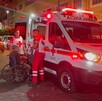 Ambulancia y tres paramédicos de la Cruz Roja atendiendo a un adulto mayor en silla de ruedas con personas y autos alrededor