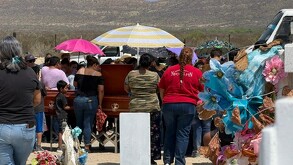 Se observa a varias personas paradas frente a un ataúd color café.