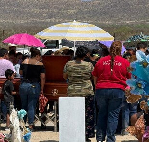 Se observa a varias personas paradas frente a un ataúd color café.