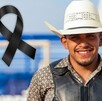 Se observa a un hombre joven que porta un sombrero vaquero y está sonriendo, hay un moño negro a lado.