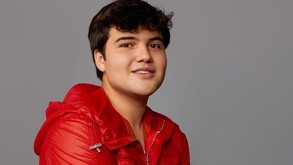 Creador de contenido Jair Sánchez viendo a la cámara mientras viste un traje color rojo delante de un fondo plano color café