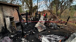 Restos calcinados de una casa con electrodomésticos, colchas y escombros dentro de un área acordonada por cintas policiacas
