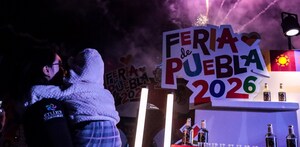 una mujer carga a un niño mientras hay fuegos artificiales y el logo de la feria de puebla 2026