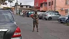 Hombre con ropa militar porta un arma mientras vigila en la vía pública.