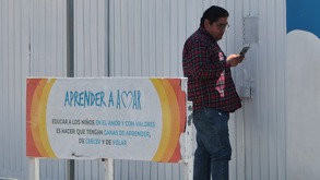 Hombre con celular en la mano afuera de una escuela.