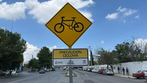Se observa un letrero color amarillo que dice ciclovía, atrás está la calle.