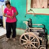 Se observa a una mujer de la terecera edad con playera rosa y agarra una silla de ruedas.
