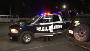 Es de noche, se observa una patrulla y unas personas abajo de la patrulla de policía.