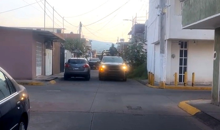Camioneta del Ejército Mexicano con militares a bordo transitando calles de Uruapan con casas y auto alrededor