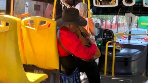 Hombre mayor con la cara bluerada tocando su guitarra mientras está sentado a bordo de un camión de la ruta 52 en Guadalajara con muletas a un lado