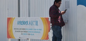 Hombre con celular en la mano afuera de una escuela.
