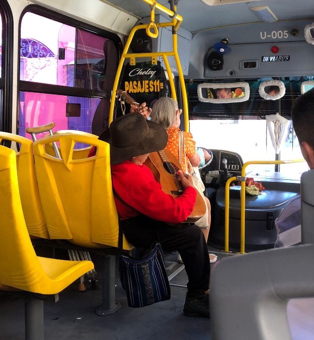 Hombre tocando su guitarra mientas va sentado en un camión de Guadalajara con sus muletas a un lado y demás pasajeros alrededor