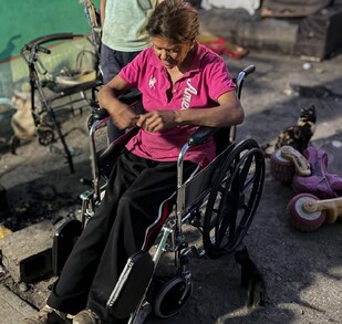 Se observa a una mujer de la tercera edad en una silla de ruedas; viste una blusa color rosa.