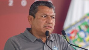Hombre de avanzada edad y rostro reacio hablando ante un micrófono.