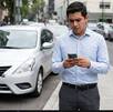 Un joven de camisa azul frente a un auto mientras observa su teléfono celular con preocupación