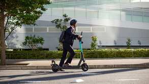 Un hombre conduciendo un scooter en una ciudad visto de perfil