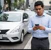 Un joven de camisa azul frente a un auto mientras observa su teléfono celular con preocupación