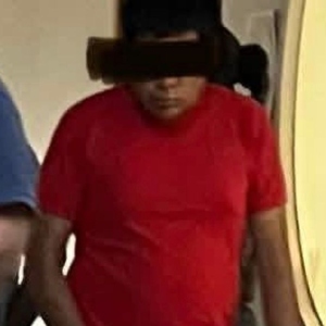 un hombre con una playera roja y pantalones café detenido